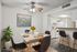 Beautifully staged dining area with a modern table set for four, vibrant sunflower centerpiece, and adjacent open kitchen. Elegant decor with floral artwork and lush green plant enhancing the cozy atmosphere.