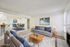 Inviting living and dining area with modern furniture, featuring a cozy gray sofa, elegant dining set, and bar seating in a contemporary open-plan design with natural light.