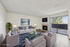 Bright and inviting living room with modern decor, plush gray sofas, and a cozy fireplace, enhanced by natural light through large sliding glass doors.