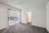 Bright and airy room with plush carpet, sliding glass door leading to a balcony, and a cozy corner leading to another room.