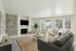 Bright and inviting living room with a large window view, featuring a cozy fireplace, elegant gray sofa, and modern armchairs, perfect for relaxation and entertaining.