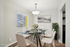 Elegant dining area with a modern glass table set for six, featuring chic white chairs, a stylish chandelier, and bright natural lighting from a large window.