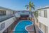 Charming apartment courtyard with a sparkling blue kidney-shaped pool surrounded by sunlit modern buildings and lush palm trees, perfect for relaxation.