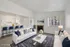 Modern open-concept living room with cozy fireplace, elegant white sofas, and stylish kitchen with bar seating, accented by tasteful decor.