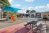Charming apartment community featuring a vibrant playground with slides, a sparkling swimming pool, and cozy picnic area under blue skies.