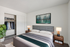 Elegantly staged bedroom featuring a plush gray headboard, modern bedside lamps, stylish artwork, and an organized open closet.