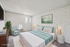 Elegant bedroom featuring a plush bed with teal accents, modern artwork, and natural light from vertical windows for a serene ambiance.