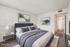 Modern bedroom with plush gray bed, textured accent wall, and elegant artwork, creating a cozy retreat.