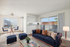 Bright, virtually staged living and dining area featuring elegant furniture, a cozy navy sofa, and abundant natural light from a large window overlooking the balcony.