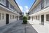 Charming apartment complex with a modern courtyard, featuring sleek black railings, large windows, and a lush central plant under a bright blue sky.