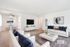 Bright and airy living room with elegant white sofas, plush blue accents, and modern art, leading to a cozy dining area.