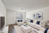 Virtually staged modern living room with sleek white sofas, blue accent pillows, abstract wall art, and a cozy shag rug creating a welcoming atmosphere.