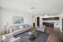 Modern living room with elegant gray sofas, contemporary glass coffee table, and open-concept kitchen featuring sleek dark cabinetry and classic appliances.