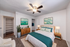 Elegant bedroom featuring modern decor with a plush bed, stylish wooden furniture, and calming green artwork, accentuated by ample natural light and a ceiling fan for comfort.