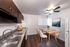 Chic kitchen with modern dark cabinets, dual sink, and elegant dining area featuring a wooden table and plush chairs, enhanced by ambient ceiling fan lighting.