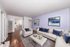 Chic living room with elegant white sofas accented by blue cushions, featuring a beautiful pastel wall and contemporary art, leading into a bright dining area.