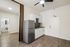 Modern apartment interior showcasing a sleek kitchenette with white cabinetry, stainless steel fridge, and stylish backsplash, adjacent to a bright bathroom entrance.