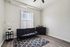Bright and modern living room featuring a sleek black sofa, elegant rug, and large window with vertical blinds. Minimalistic decor enhances spacious feel.