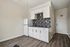 Modern kitchen with sleek white cabinetry, stylish backsplash, and elegant wood flooring in a bright apartment.