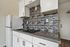 Modern kitchen with sleek gray countertops, elegant mosaic tile backsplash, and crisp white cabinetry.