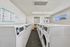 Bright and modern apartment laundry room with rows of white washers and dryers, spacious layout, and natural lighting from large windows.