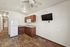 Inviting apartment kitchen with elegant wood flooring, sleek white appliances, rich cabinetry, and a mounted flat-screen TV.