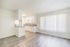 Bright, modern open-concept kitchen and living area with sleek flooring and large window with vertical blinds.