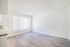 Bright and modern living space featuring sleek hardwood floors, large window with vertical blinds, and fresh white walls, perfect for a contemporary lifestyle.