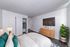 Modern bedroom with cozy bed, stylish dresser, mounted TV, and elegant indoor plant, perfect for relaxation.