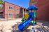 Charming apartment exterior with a vibrant children's playground featuring a colorful slide and secure fencing, perfect for families.