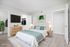 Bright and modern bedroom featuring elegant decor, a comfortable bed with teal accents, sleek furniture, and a flat-screen TV, offering a serene and stylish retreat.