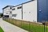 Modern apartment exterior with clean white and blue design, surrounded by a well-kept fence and green lawn, offering a stylish and inviting living space.
