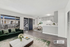 Chic open-concept living space with elegant green velvet couch, modern kitchen, and inviting dining area, enhanced by abundant natural light.