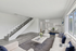 Modern living room with stylish staircase, cozy seating, and natural light, leading to a sleek kitchen area.