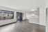 Bright and spacious living area with modern gray flooring and a sleek kitchen, featuring ample natural light from large windows.