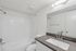 Modern bathroom featuring a sleek vanity with a stylish faucet, bright wall lighting, and a pristine white bathtub surrounded by subway tiles.