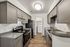 Modern kitchen with sleek gray cabinetry, stainless steel appliances, and hardwood flooring, leading to an in-unit laundry area.