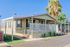 Charming mobile home with spacious porch, surrounded by lush greenery and a sunny, peaceful neighborhood setting.