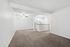 Bright living area with plush carpeting and open access to a modern kitchen, featuring a ceiling fan for added comfort.
