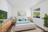 Bright and airy virtually staged bedroom featuring a plush bed, modern wooden furniture, and a large window with lush greenery outside.
