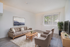 Inviting living room with modern decor, featuring a plush sofa, stylish armchairs, and a scenic wall art. Natural light streams through large windows, enhancing the elegant simplicity.