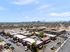 Aerial view of a vibrant apartment complex with palm tree-lined streets, ample parking, and a glimpse of the city skyline under a clear blue sky.