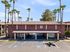 Inviting two-story residential building with a charming red tile roof surrounded by tall palm trees, featuring accessible parking spaces under a clear blue sky.