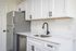 Newly renovated kitchen with white sharker cabinets, wood-inspired flooring, white hard-surface countertops, black fixtures, stainless steel appliances, and a farmhouse-style sink