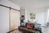 Modern Apartments in Downtown Portland, OR - ORO - Furnished Living Room With Wood-Style Floors, Barn-Style Sliding Door, A Large Window, A Dining Area, And A Kitchen With Stainless Steel Appliances