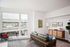 Pearl District, OR, Luxury Apartments - ORO - A Living Room with a Leather Sofa, Accent Chair, Large Window, Floor Lamp, Sideboard Cabinet, and a Potted Plant.