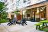 Apartments in Woodstock, OR, with Air Conditioner - Novus - A Firepit with Outdoor Seating, String Lights, Landscaped Greenery, and an Adjacent Indoor Lounge Space.