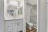 Apartments in South Reno, NV - Redfield Ridge - Modern Bathroom With Single-Sink Vanity, Round Mirror, Brushed Nickel Faucet, and Glass-Enclosed Shower With Marble-Look Tile.