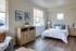 Albany, OR, Apartments - Creekside Meadows - Bedroom with Light-Colored Walls and Dark Wood Floors, Nightstands Flanking the Bed with a Lamp and Dresser, Potted Plants, Sofa, and Large Windows.