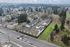 Aerial drone shot of property and surrounding area showing woodland with lots of trees, roads, gas station, and other local businesses as well as long horizon shot of woods and clouds.
